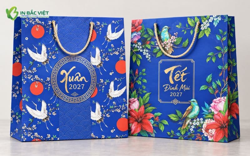 Hai mẫu túi giấy quà Tết 2027 màu xanh dương với họa tiết chim hạc, hoa lá và thiết kế nghệ thuật nổi bật